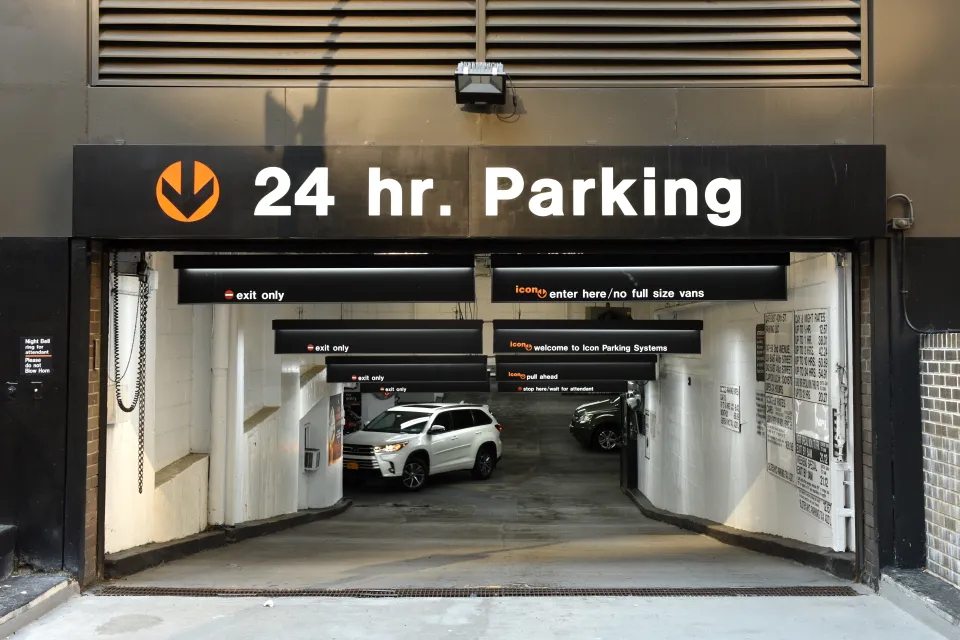 24-hour parking sign above parking garage entrance through which you can see a white SUV driving